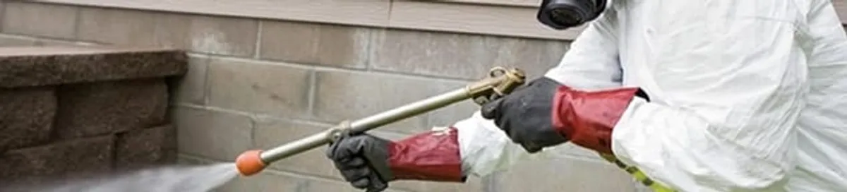 Pest control technician applying exterior insect treatment along a home foundation in Erie, PA