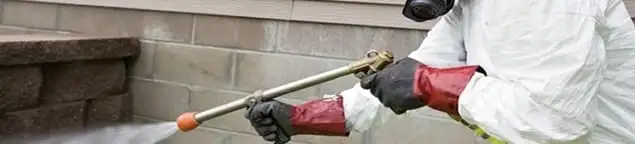 Pest control technician applying exterior insect treatment along a home foundation in Erie, PA
