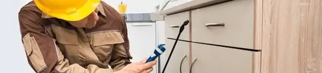 Roach exterminator applying treatment under kitchen cabinets in Erie, PA