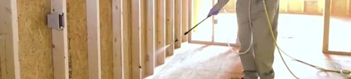 Termite treatment technician applying spray along framing and unfinished walls in Erie, PA